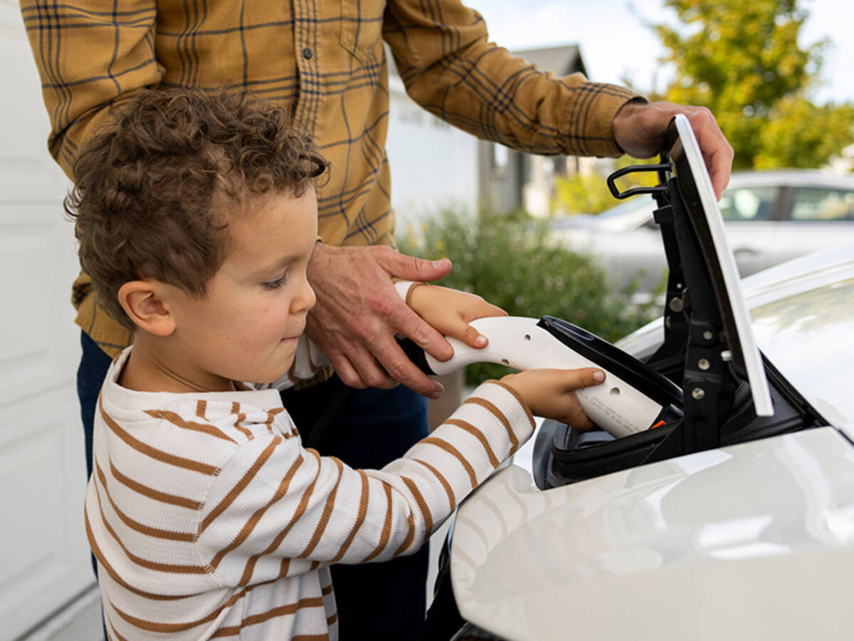 Young child plugging a charger into an electric vehicle at home with a parent’s help