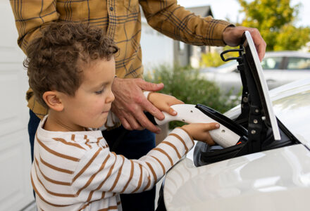 Young child plugging a charger into an electric vehicle at home with a parent’s help